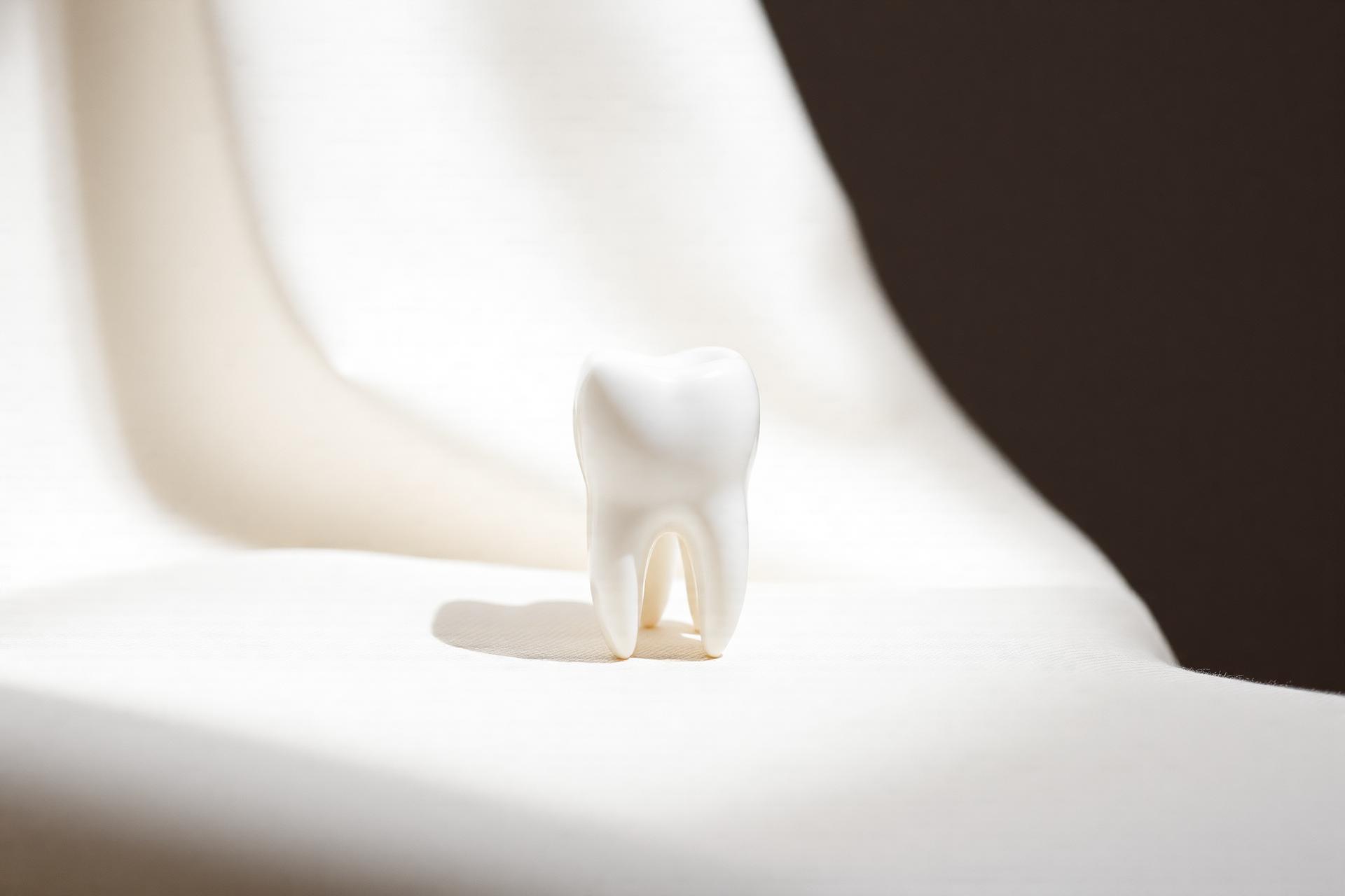 A porcelain tooth resting on ivory linen in soft daylight